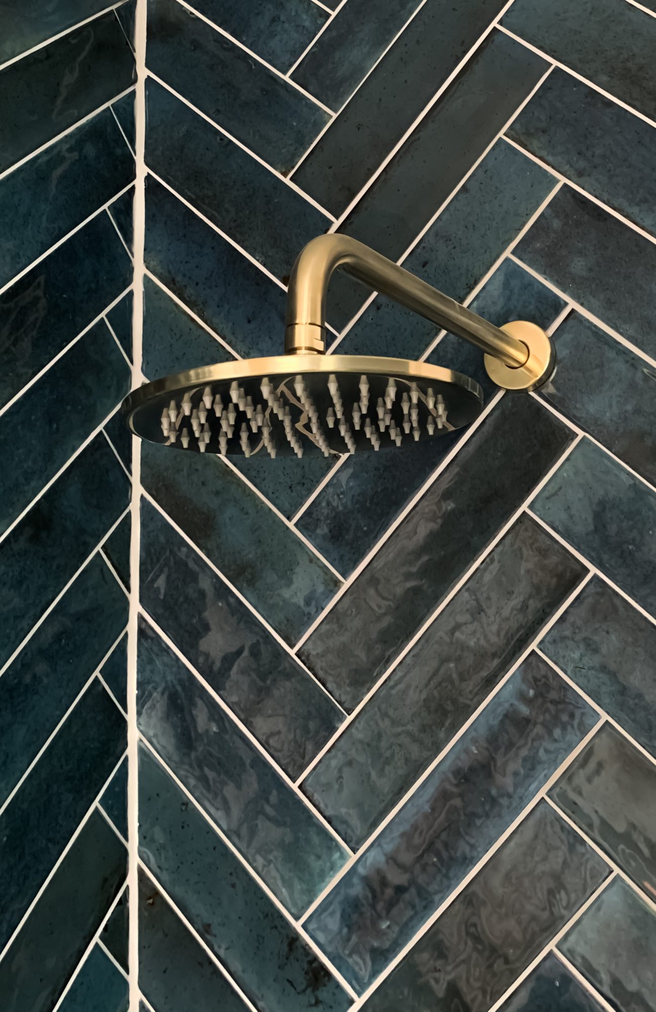 A brushed brass shower head on teal herringbone tiles